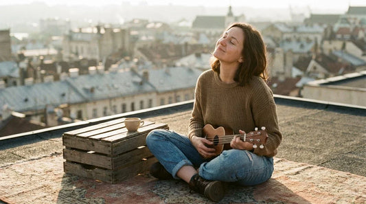 Woman playing soprano ukulele outdoors with eyes closed, music mental health wellbeing