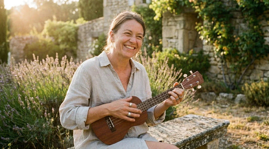 Older woman smiling playing soprano ukulele outdoors in sunlight, senior beginner